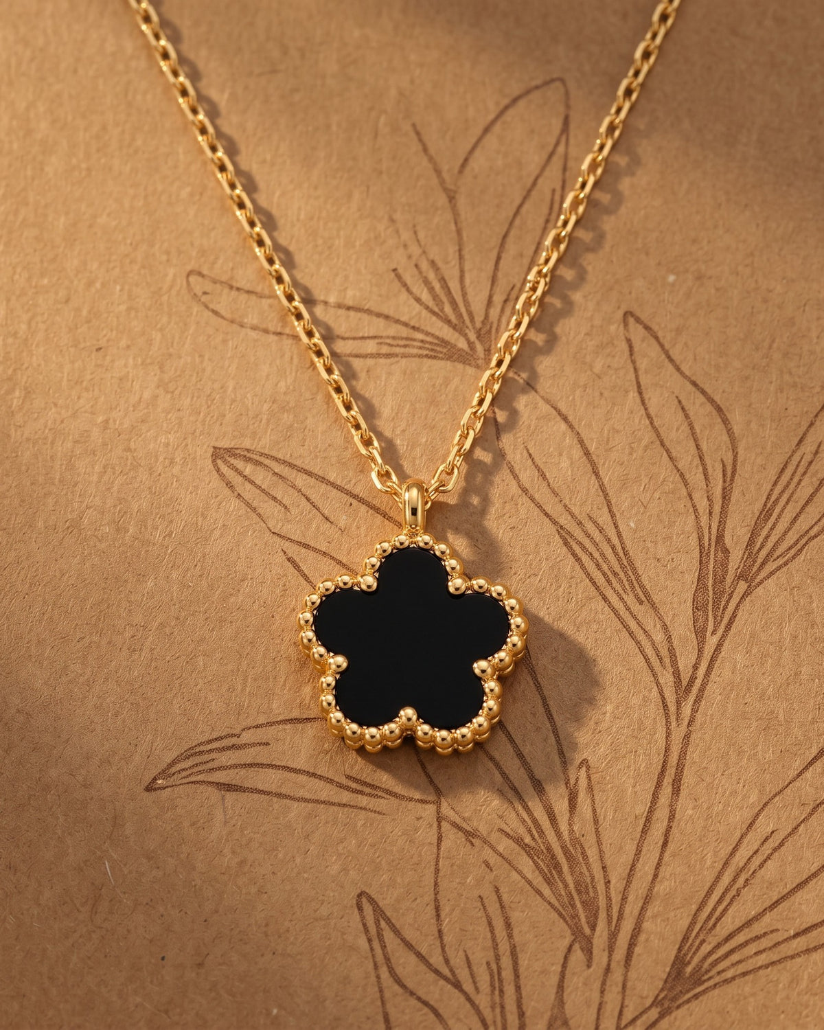Gold-tone black flower pendant necklace laid flat on kraft paper